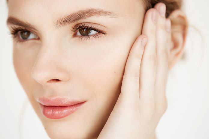 Close up of young beautiful girl smiling touching face over white background. Spa beauty health and cosmetology concept.