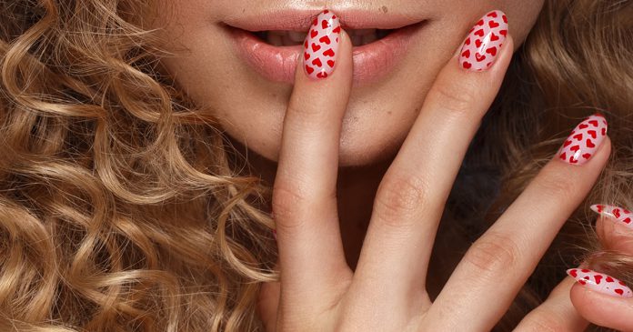 Pretty girl with curls hairstyle, classic makeup, freckles, nude lips and manicure design with hearts. Beauty face. The image for Valentine's Day