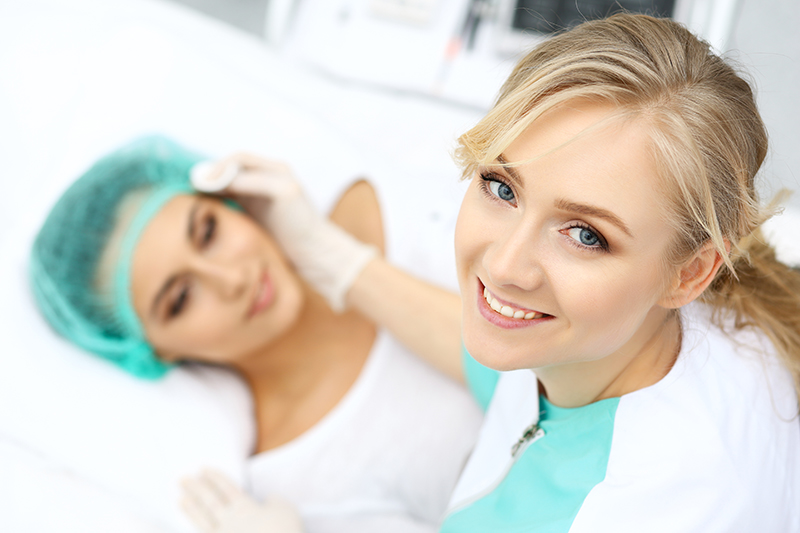 Uśmiechnięta lekarka medycyny estetycznej przygotowuje pacjentkę do zabiegu.